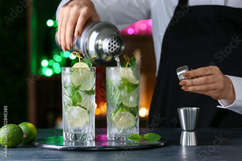 Female bartender making fresh mojito on table in bar