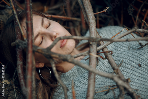 Teenager young woman lying outdoor in the park under dry tree branches. Sex maniac crime rape violence concept photo