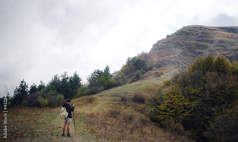 man with backpack and sticks for trekking hiking in the mountains. The beginning of autumn season. Beautiful foggy weather