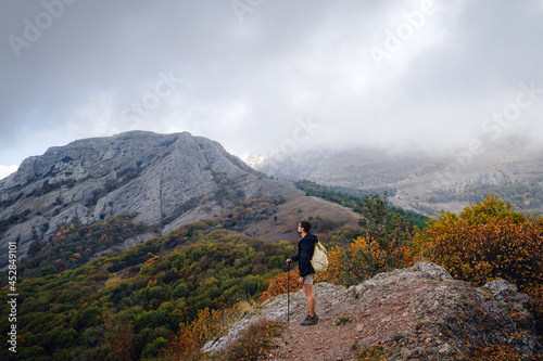 man with backpack and sticks for trekking hiking in the mountains. The beginning of autumn season. Beautiful foggy weather