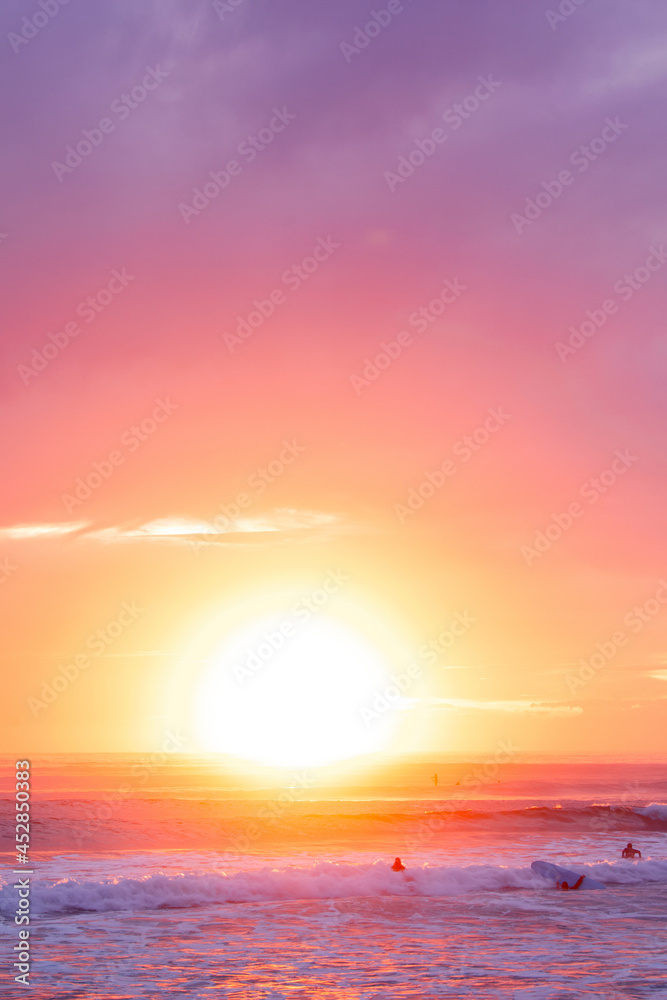 Sunlit sky ocean sunrise with surfers