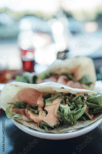 Close up shot of a Piadina sandwich, a typical italian flatbread, in a busy bar in Milan during aperitif hour. The piadina is filled with prosciutto ham, arugula and pink salsa. photo