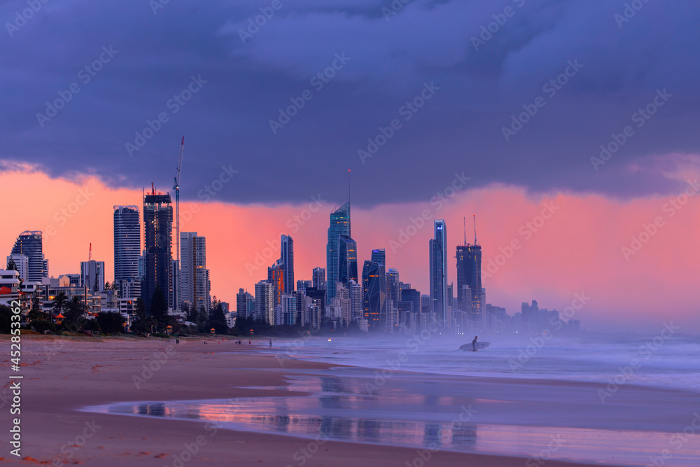 Storm clouds over Surfers Paradise cityscape, with surfers going into the ocean