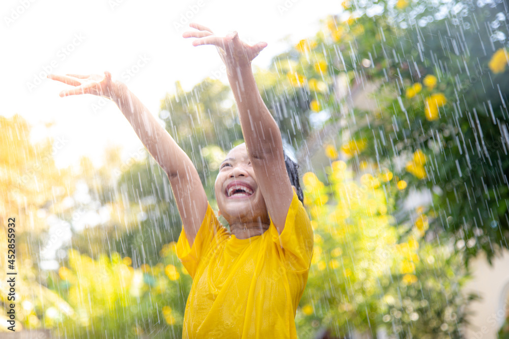 Happy Asian little child girl having fun to play with the rain in the sunlight