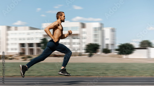 A young man with a naked torso is running fast through the stadium against the backdrop of a building