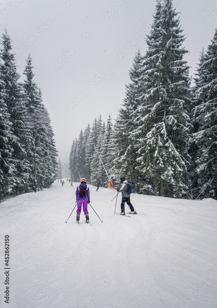 People skiing on the snowy slope of Bukovel ski resort in the Ukrainian Carpathian mountains. Snow falling scene, blizzard frosty weather.