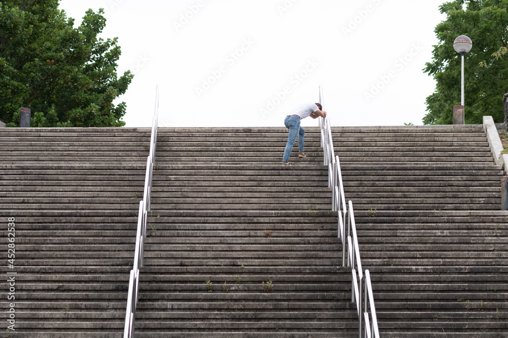 Tired man climbing stairs just before reaching the top. Hard way to success and achieving goals concept Tired man climbing stairs just before reaching the top. Hard way to success and achieving goals concept