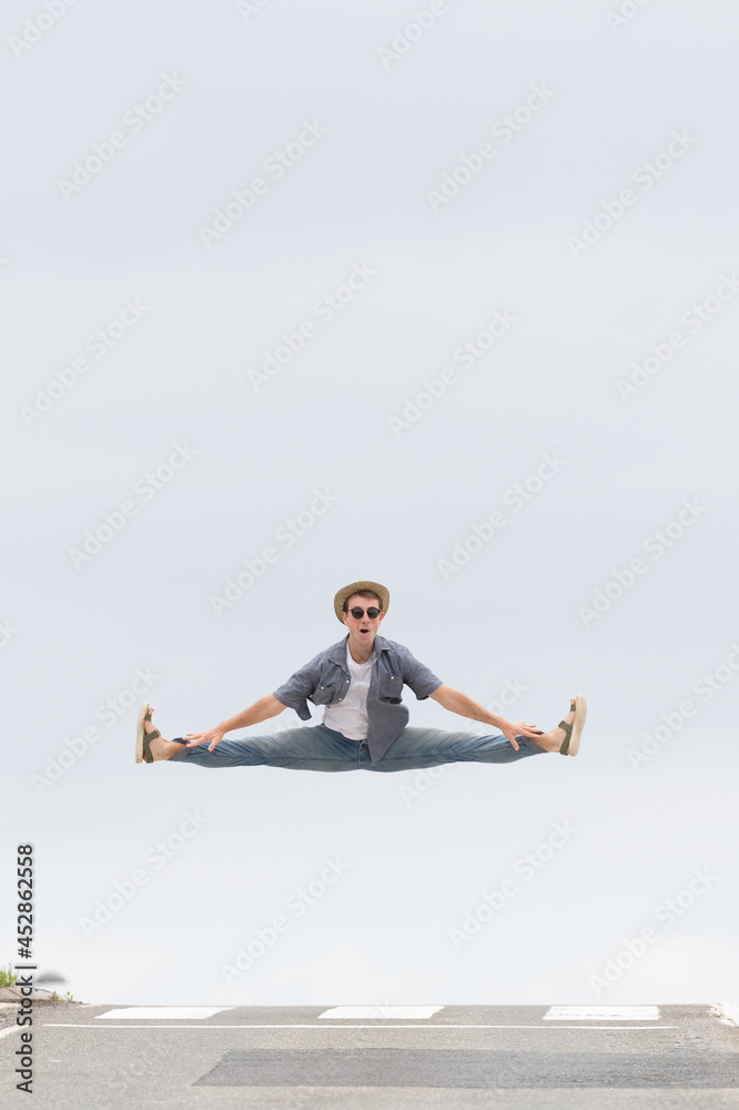 Happy casual dressed male dancer jumping on the road. Happiness concept with copy space. Minimal composition with asphalt and sky
