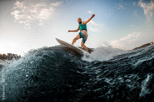 sportive man on turquoise lifejacket is surfing on surfboard on the river © fesenko