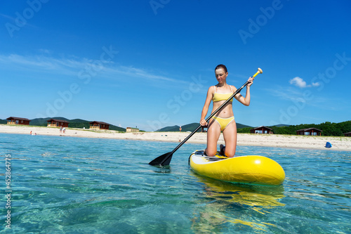 Woman stand up on paddle board in sea. Big yellow board in turquoise water.