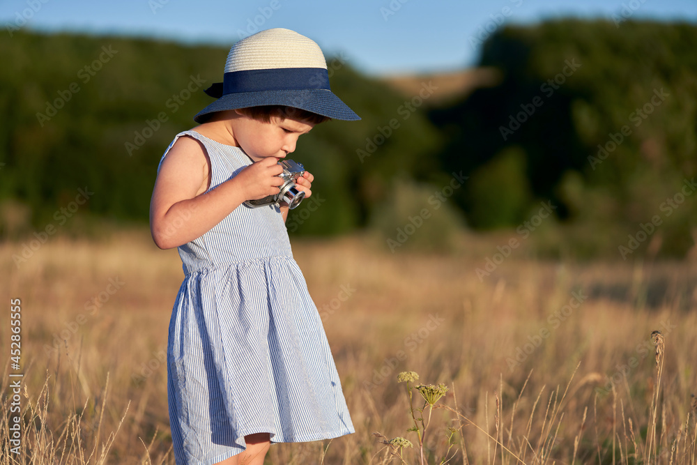 Portrait of a little girl with a camera in nature in the rays of the setting sun. The baby chooses an object in the grass for shooting. Copy space. Selective focus. Portrait of a little girl with a camera in nature in the rays of the setting sun. The baby chooses an object in the grass for shooting. Copy space. Selective focus.