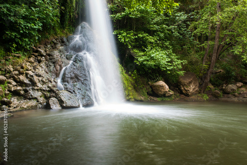 Una cascada cae sobre unas rocas y un lago en medio del bosque en una foto de larga exposición