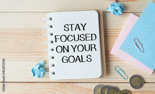 Inspirational quote - Stay focused on your goals. With text message on white paper book and coins.