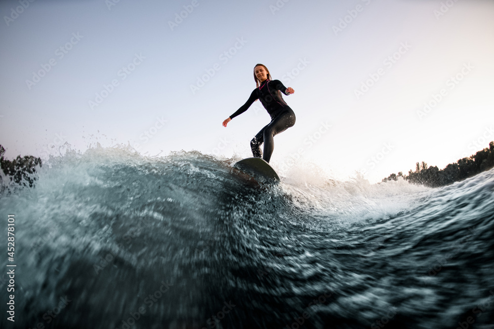athletic female wakesurfer balanced on the board on river wave
