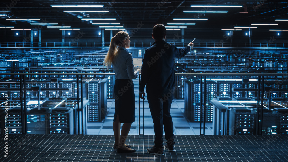 Obraz premium Data Center Male It Specialist and Female e-Commerce Manager Talk, Use Laptop. Big Server Farm Cloud Computing Facility with Information Technology Professionals Working.