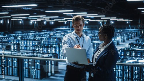 Data Center Female System Administrator and Male IT Specialist talk, Use Laptop. Information Technology Engineers work on Cyber Security Protection in Cloud Computing Server Farm.