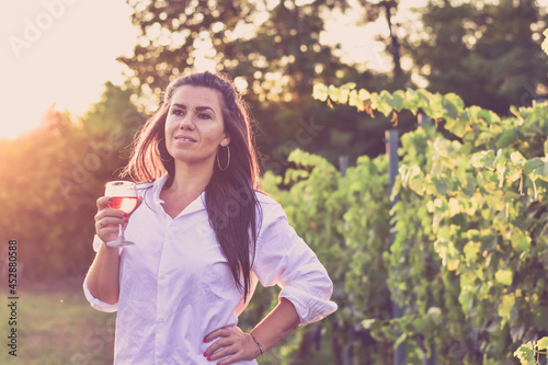 Young beautiful Happy smiling Brunette Woman walking at Vineyard with a glass of rose wine.Wine tourism