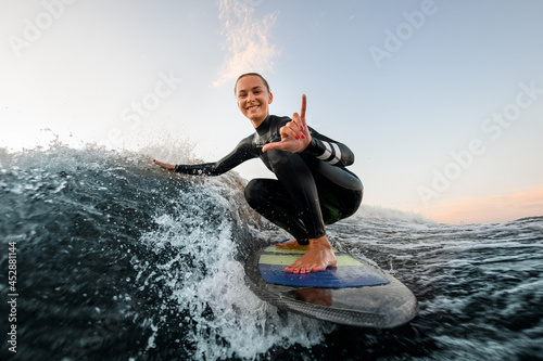 smiling woman sits on wakesurf board and rides the wave and touches the waves with one hand photo
