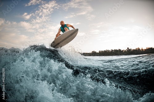 amazing view of splashing wave and man skilfully jumping over it on wakeboard