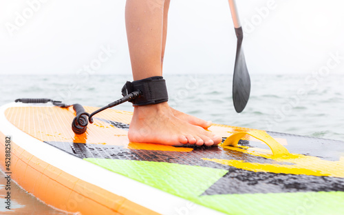 Stand up paddle board on a sea lake, close-up of legs with a safety rope. Person on a SUP. Paddle Boarding, water sports. Active healthy lifestyle, digital detox. Traveling, summer vacation.