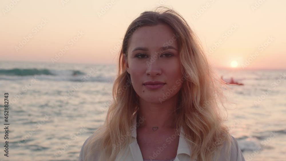 Young blonde woman with wavy hair standing on beach by the sea on sunset Young blonde woman with wavy hair standing on beach by the sea on sunset