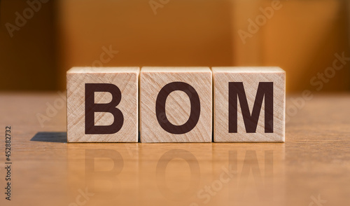 BOM - bill of materials, text on wooden cubes on orange wall background.