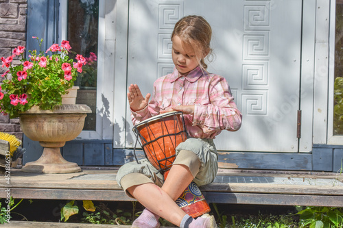 the girl child with a djembe drum outdoor on the porch of the house photo without processing