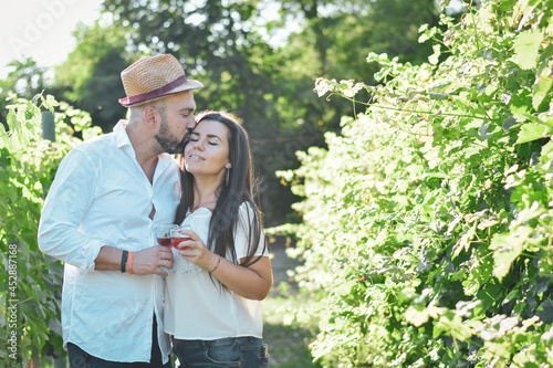 Portrait of a smiling  happy couple kissing    in a Vineyard toasting wine. Beautiful  brunette woman and bearded muscular man spending time together © Striker777