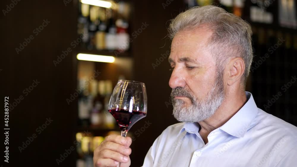 An elderly, bearded, gray-haired, well-dressed sommelier, a male winemaker, tastes the aroma and checks the quality of red wine Winemaking concept. Senior sommelier tasting red wine. Close-up An elderly, bearded, gray-haired, well-dressed sommelier, a male winemaker, tastes the aroma and checks the quality of red wine Winemaking concept. Senior sommelier tasting red wine. Close-up