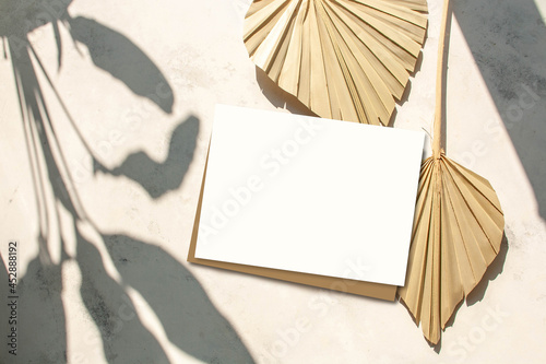 Dry palm leaves and blank greeting card mock up scene on a cement background and contrasting shadows. Flat lay, top view. Empty space. Modern still life