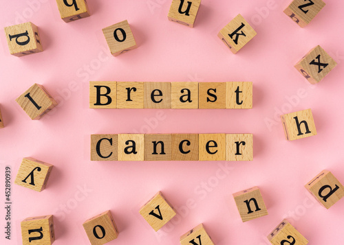 Breast Cancer word on wooden block. Flat lay view on light pink background.