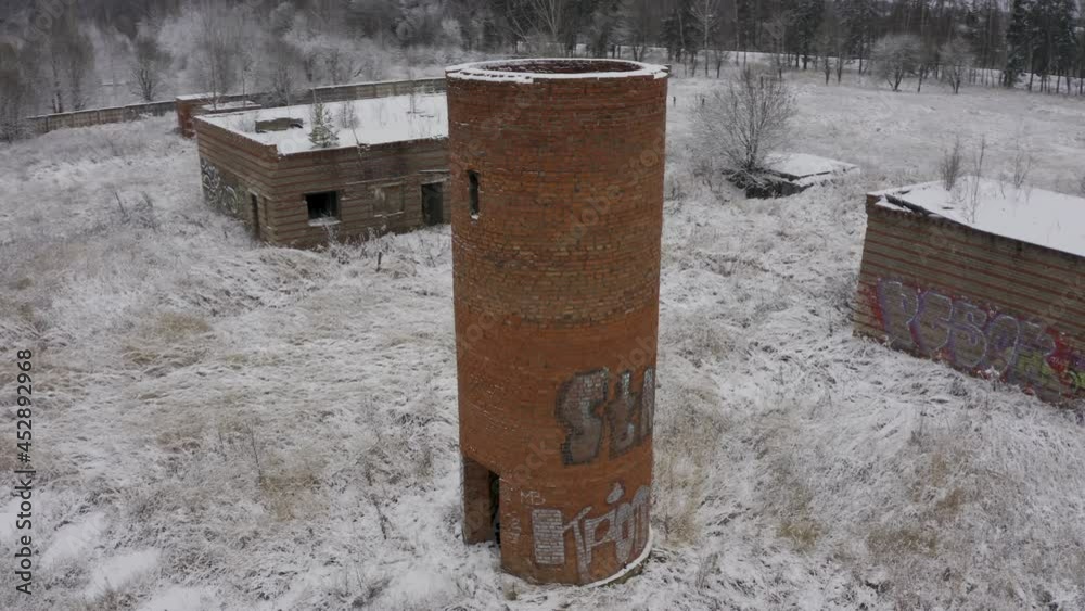 A brick abandoned water tower in the middle of a forest and abandoned buildings in a winter landscape. air view A brick abandoned water tower in the middle of a forest and abandoned buildings in a winter landscape. air view