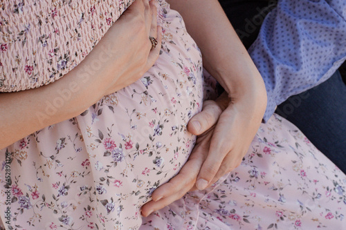 2 pairs of hands embracing a pregnant woman's stomach. 