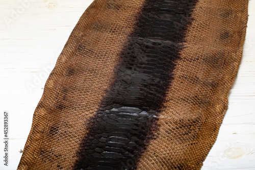 Obraz na plátně Brown dyed folded natural genuine python leather on the wooden table