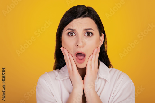 Portrait of speechless shocked girl palms cheeks open mouth on yellow background