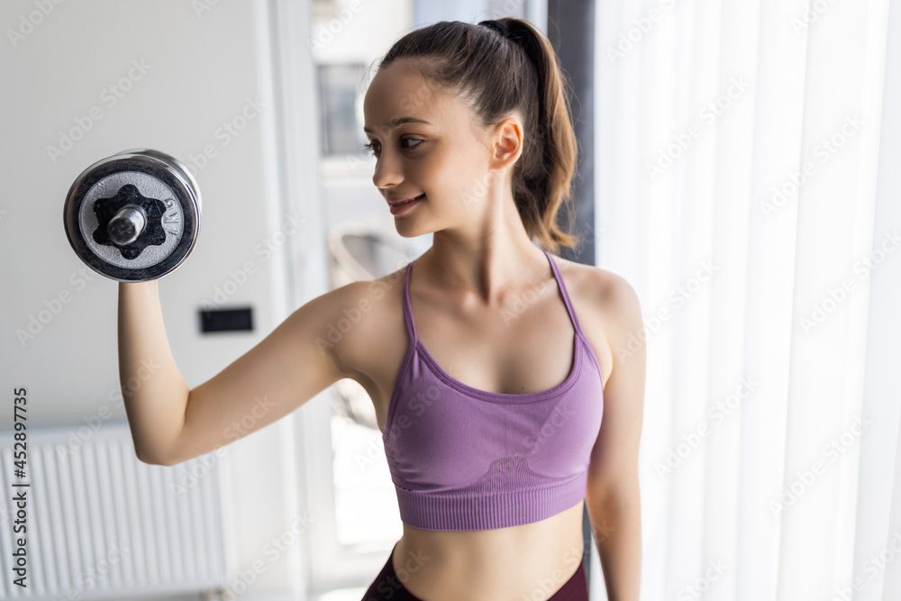 Sporty woman exercising with dumbbell at home to stay fit