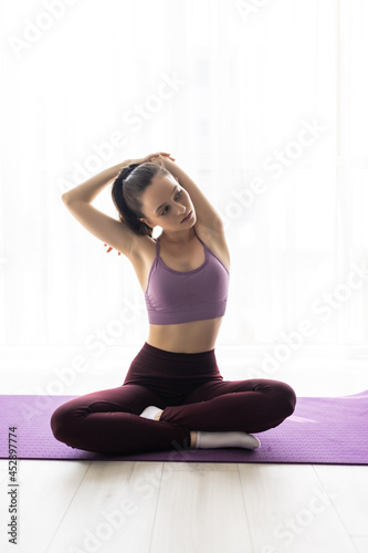 Young attractive smiling woman practicing yoga, sitting in Half Lotus exercise, Ardha Padmasana pose, working out, wearing sportswear, meditation session, indoor full length, home interior
