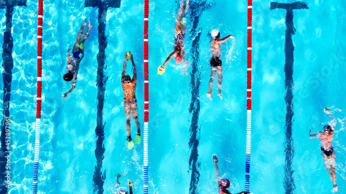 Top view of group of young swimmers training in swimming pool with marked lanes outdoor. Many sportive people and kids swim in Open Water Swimming pool with clean blue water. Summer sports camp photo