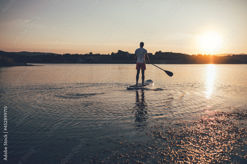 Rear view of man paddleborading at sunset