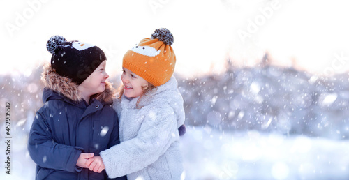 A little boy and a girl hugging and smiling under the snow in the forest