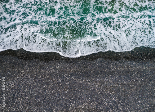 Stormy weather, sea waves breaking on a shore with volcanic black sand, background with copy space