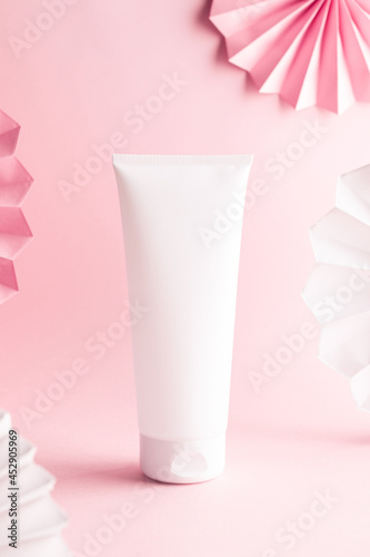 White cream tube on a pink background. decorated with paper garland, mock up image © Татьяна Медведцкая