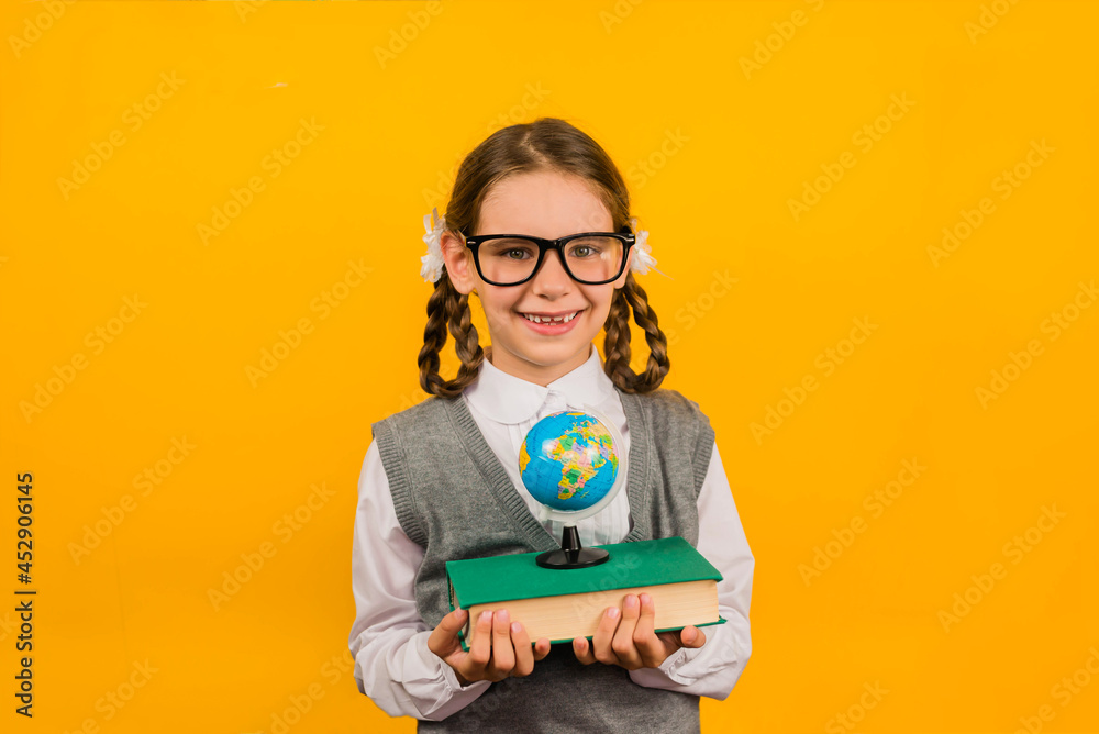Back to school kid. Happy child holds a book and globe in her hand on a yellow background. Education and intellectual development of children. 1 September. Back to school kid. Happy child holds a book and globe in her hand on a yellow background. Education and intellectual development of children. 1 September.
