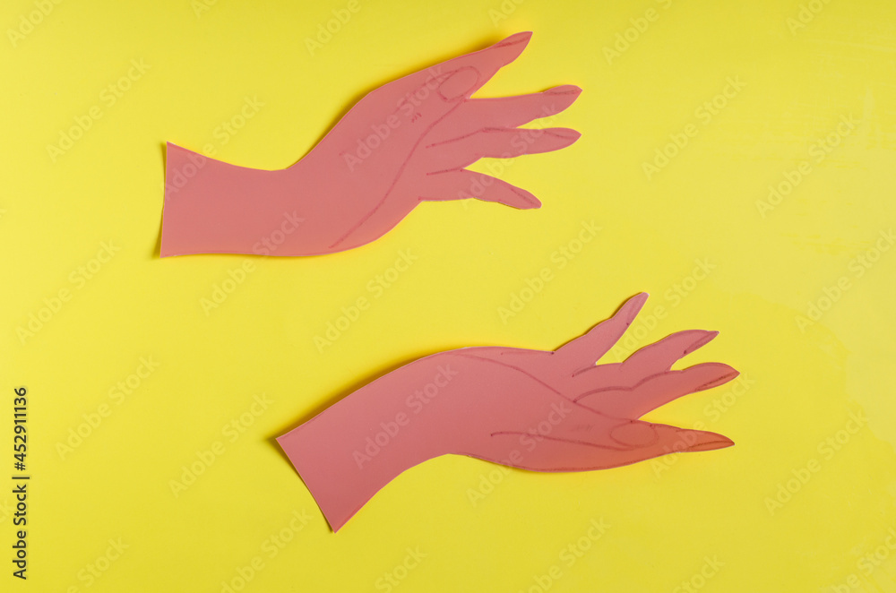 Two palms made of red paper on a bright yellow background of the mine space. The concept symbol consists of two hands holding an empty space on a colored background