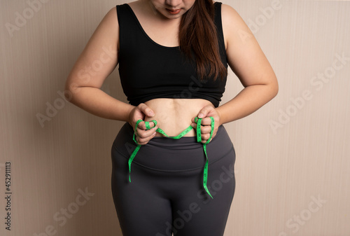 beautiful fat woman in sportswear catches her big belly or belly fat with tape measure. healthy weight control concept. overweight, bloated belly