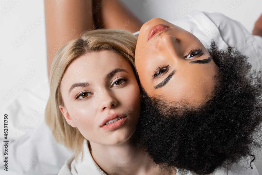 top view of african american model near blonde woman looking at camera on white top view of african american model near blonde woman looking at camera on white
