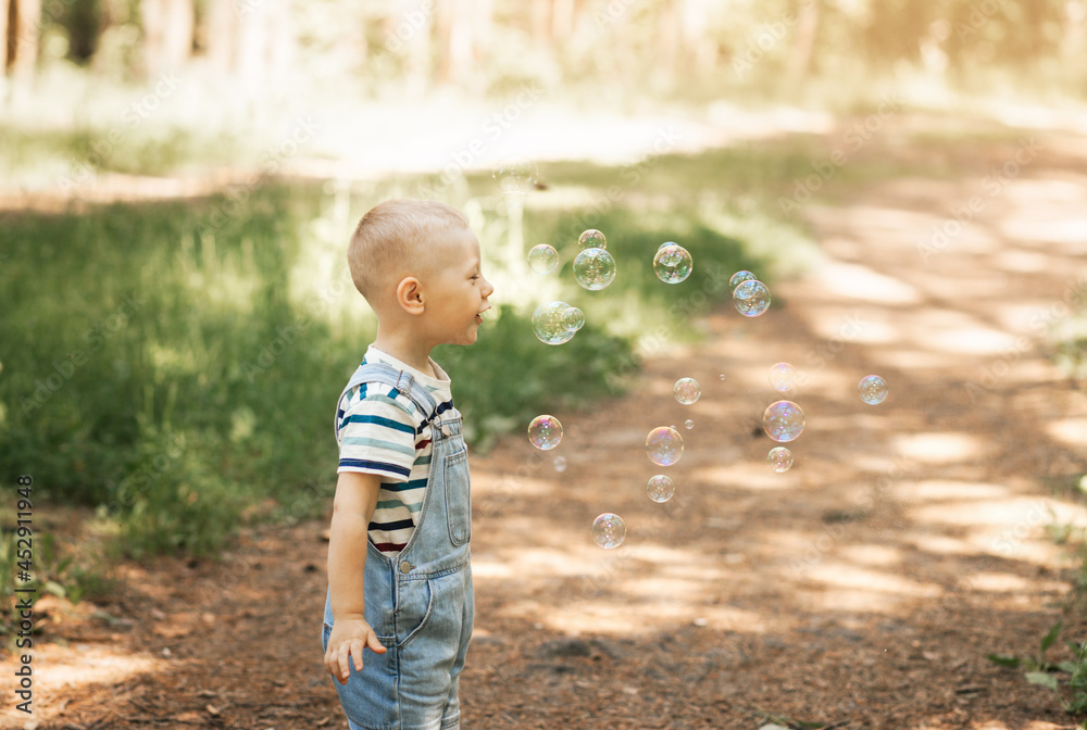 Naklejka premium Little boy inflating soap bubbles in the summer in nature