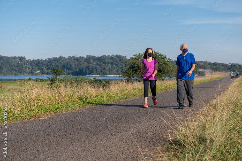 young woman and senior man wearing protective masks and walking outside on a sunny day young woman and senior man wearing protective masks and walking outside on a sunny day