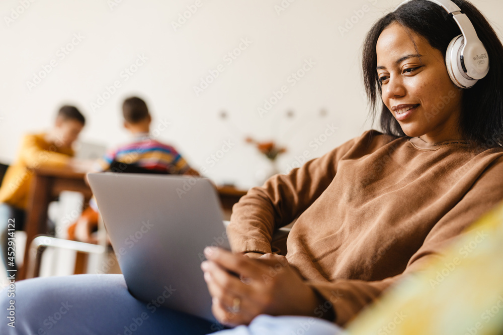 Black woman smiling and using laptop while sitting on sofa in home Black woman smiling and using laptop while sitting on sofa in home