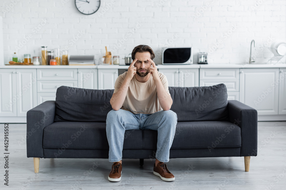 Man sitting with closed eyes on couch while suffering from headache Man sitting with closed eyes on couch while suffering from headache